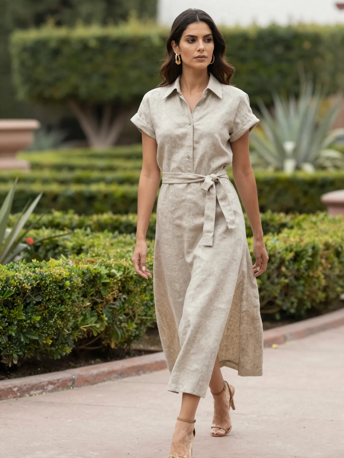A woman in a linen dress walking through a formal garden with agave